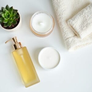 Uma visão de cima de uma bancada de banheiro organizada e chique, mostrando os dois produtos do Double Cleansing lado a lado: um frasco elegante de cleansing oil e um pote de cleansing balm, ao lado de um limpador em gel. Toalhas macias e um pequeno vaso de planta complementam a cena, sugerindo um ambiente de bemestar.